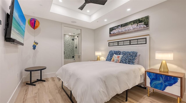 bedroom featuring ceiling fan, connected bathroom, a raised ceiling, and light hardwood / wood-style floors