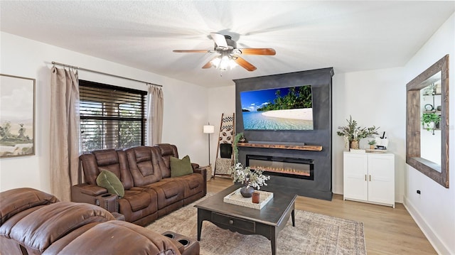 living room with light hardwood / wood-style flooring, ceiling fan, a textured ceiling, and a fireplace