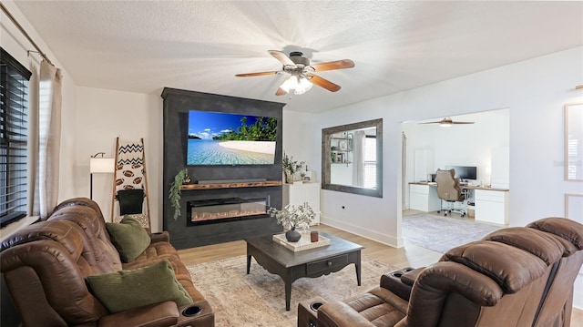 living room featuring ceiling fan, a large fireplace, a textured ceiling, and light wood-type flooring