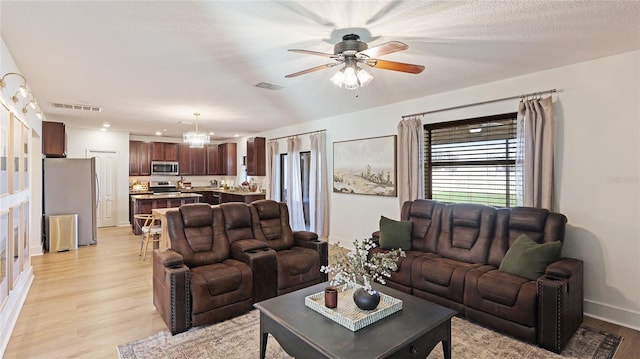 living room with ceiling fan, a textured ceiling, and light hardwood / wood-style floors