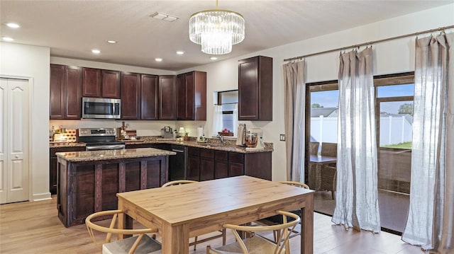 kitchen with dark stone countertops, appliances with stainless steel finishes, sink, a center island, and hanging light fixtures