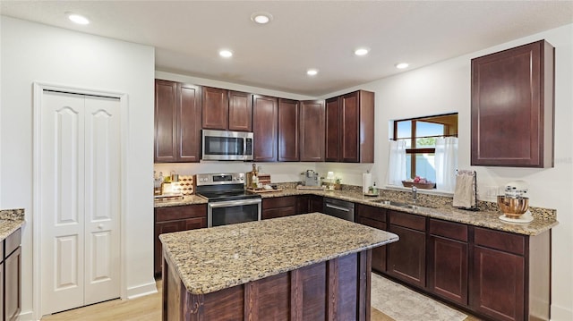 kitchen featuring light wood-type flooring, a center island, light stone countertops, sink, and appliances with stainless steel finishes