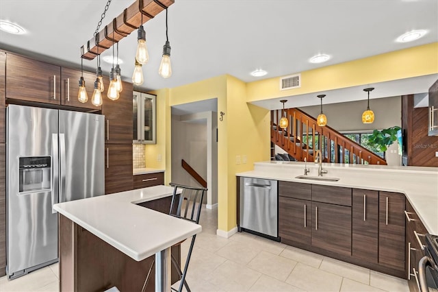 kitchen featuring sink, light tile patterned floors, hanging light fixtures, stainless steel appliances, and a kitchen breakfast bar