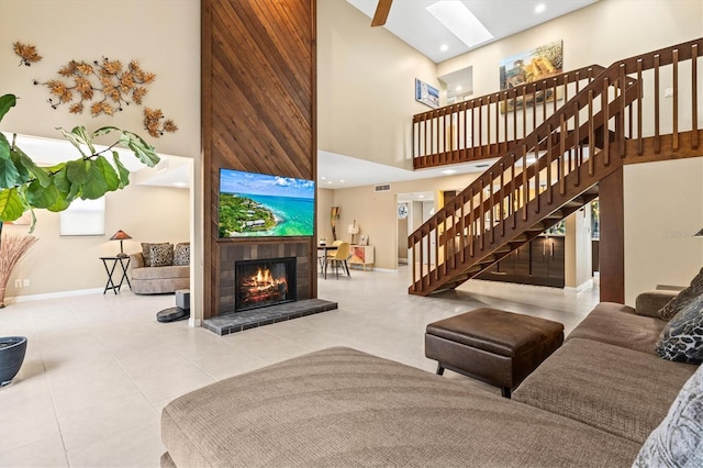 living room with a high ceiling, a tile fireplace, light tile patterned floors, and a skylight