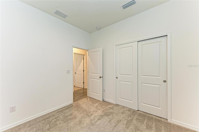 unfurnished bedroom featuring light carpet, visible vents, a closet, and baseboards