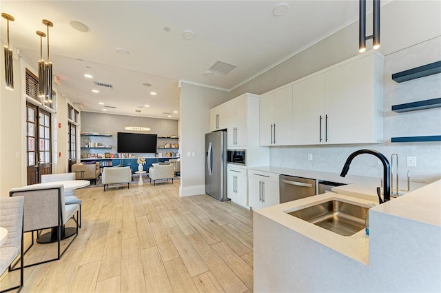 kitchen featuring light wood finished floors, light countertops, white cabinets, stainless steel appliances, and a sink