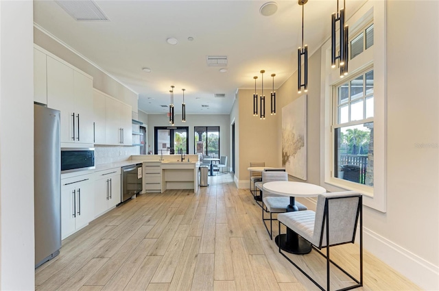 kitchen with stainless steel appliances, a peninsula, light wood-style flooring, and hanging light fixtures