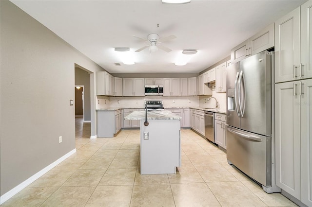 kitchen with light tile patterned flooring, sink, appliances with stainless steel finishes, a kitchen island, and ceiling fan