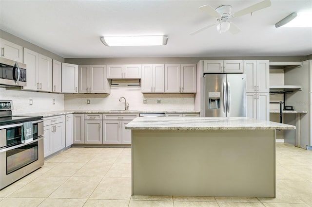 kitchen featuring light stone countertops, appliances with stainless steel finishes, a center island, and light tile patterned floors