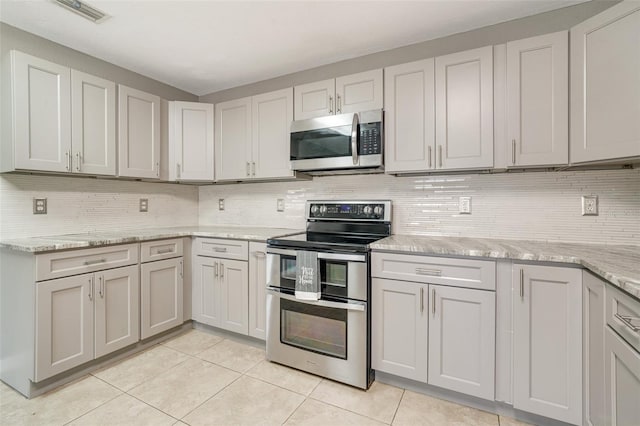 kitchen featuring light stone countertops, light tile patterned flooring, appliances with stainless steel finishes, and decorative backsplash