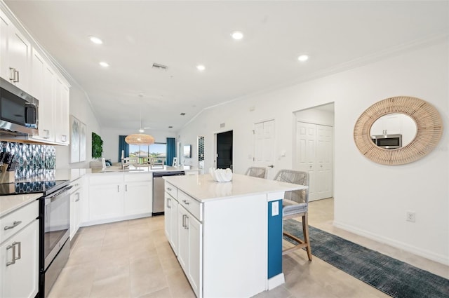 kitchen with white cabinetry, stainless steel appliances, a kitchen island, decorative light fixtures, and kitchen peninsula