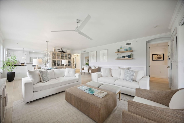 living room with crown molding, ceiling fan with notable chandelier, and light hardwood / wood-style flooring