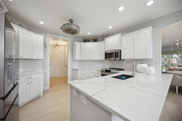 kitchen featuring sink, light stone counters, appliances with stainless steel finishes, kitchen peninsula, and white cabinets