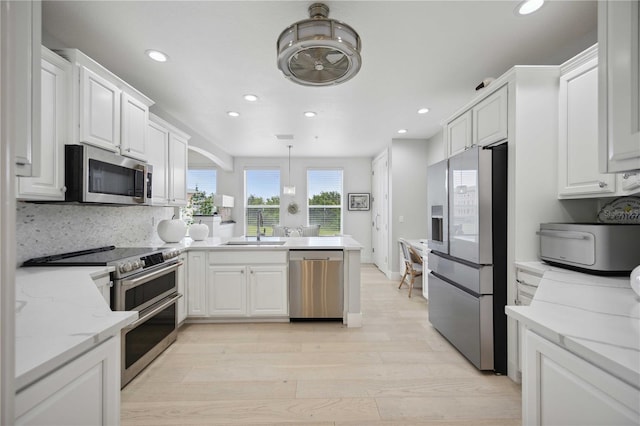 kitchen featuring sink, appliances with stainless steel finishes, light stone counters, white cabinets, and decorative light fixtures