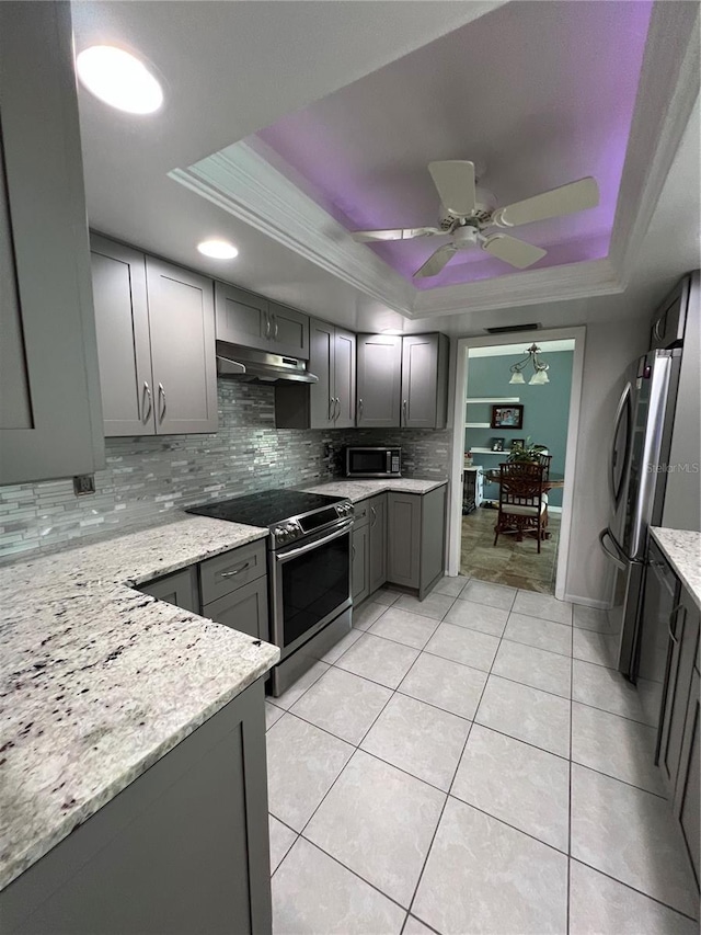 kitchen featuring a raised ceiling, appliances with stainless steel finishes, gray cabinets, and light stone counters