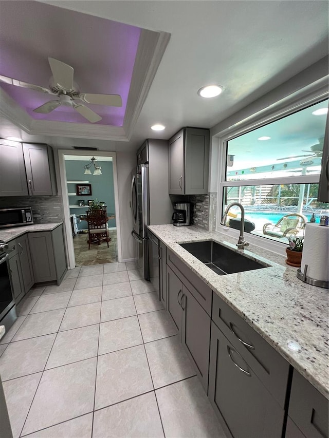 kitchen featuring sink, stainless steel fridge, light tile patterned floors, a raised ceiling, and light stone countertops