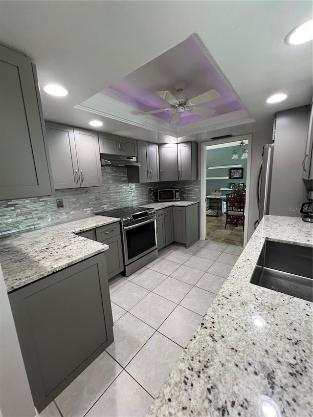 kitchen with a raised ceiling, appliances with stainless steel finishes, gray cabinetry, and light stone counters