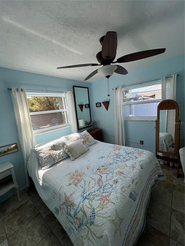 bedroom with ceiling fan, a textured ceiling, and dark tile patterned flooring