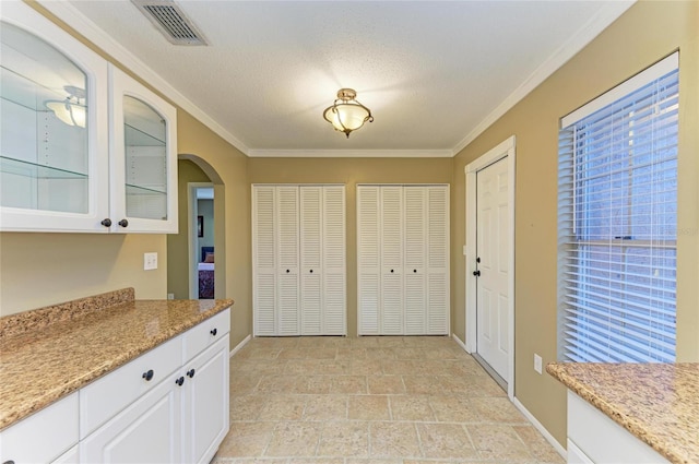 kitchen featuring white cabinetry, light stone counters, crown molding, and a textured ceiling