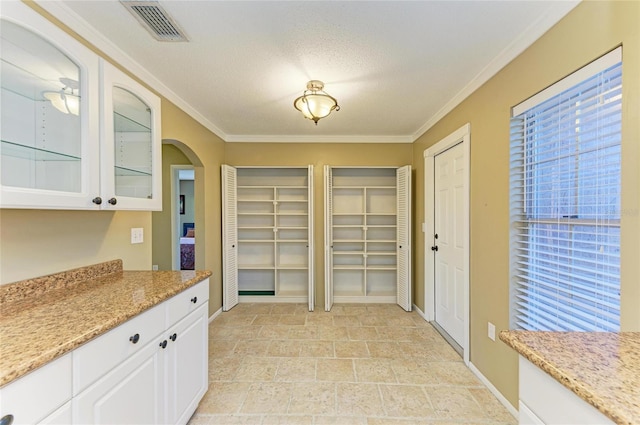 kitchen featuring white cabinetry, light stone countertops, ornamental molding, and a textured ceiling