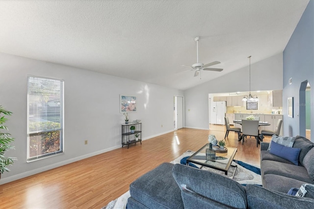 living room with hardwood / wood-style floors, ceiling fan with notable chandelier, high vaulted ceiling, and a textured ceiling