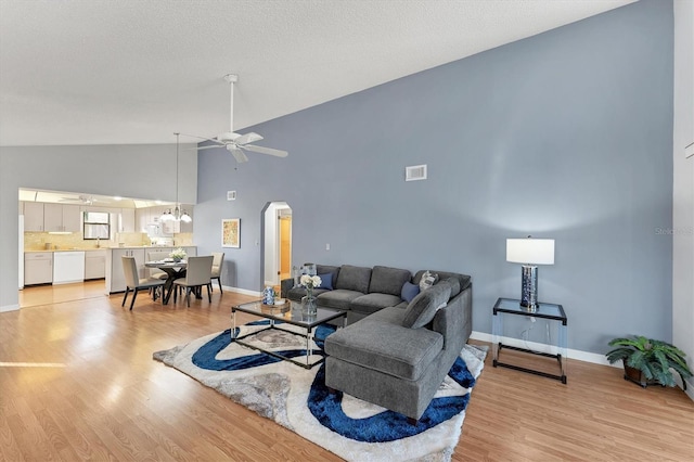 living room with ceiling fan, high vaulted ceiling, light hardwood / wood-style floors, and a textured ceiling