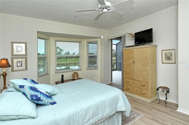 bedroom with ceiling fan, access to exterior, a textured ceiling, and light hardwood / wood-style flooring