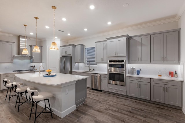 kitchen featuring appliances with stainless steel finishes, a breakfast bar, pendant lighting, a center island with sink, and wall chimney exhaust hood