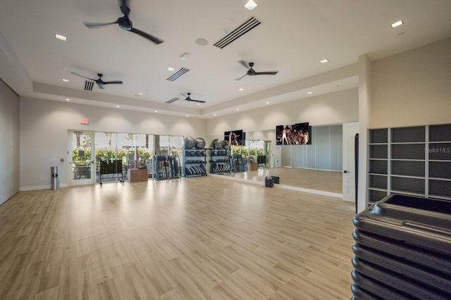 workout area with ceiling fan, a raised ceiling, light hardwood / wood-style flooring, and a high ceiling