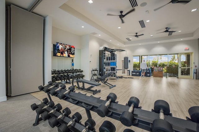 workout area featuring a raised ceiling, a towering ceiling, ceiling fan, and light hardwood / wood-style flooring