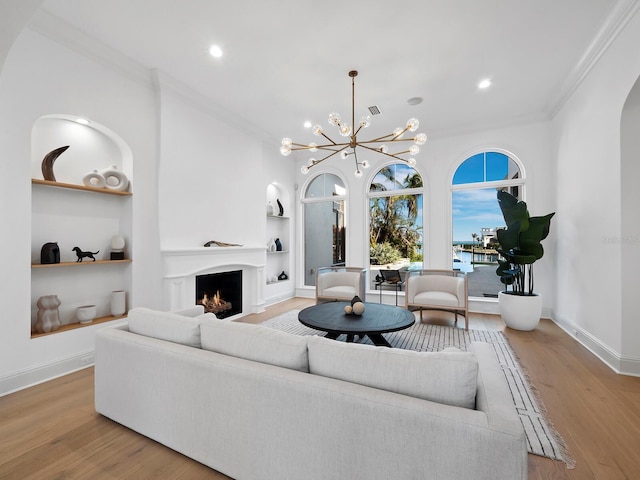 living room with crown molding, a notable chandelier, built in shelves, and light hardwood / wood-style floors