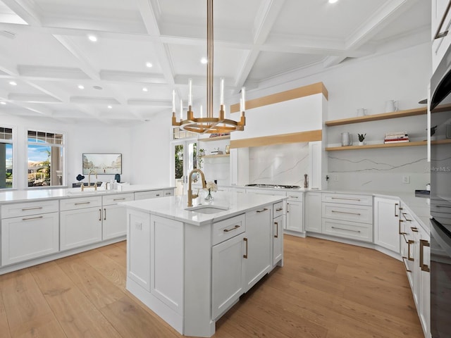 kitchen with pendant lighting, sink, white cabinetry, light hardwood / wood-style floors, and an island with sink