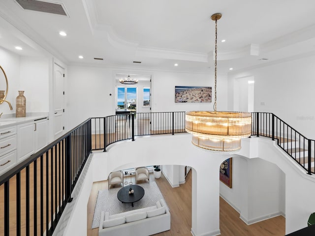 living room featuring ornamental molding, a tray ceiling, light hardwood / wood-style floors, and a notable chandelier