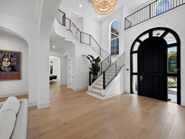 entryway with a towering ceiling, ornamental molding, light hardwood / wood-style floors, and a chandelier