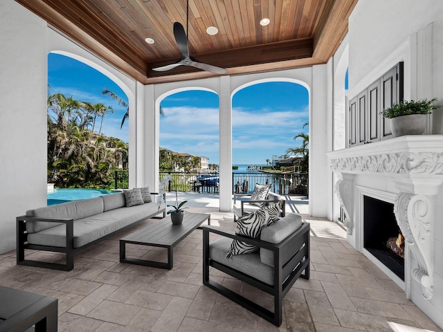 view of patio with a water view, ceiling fan, and an outdoor living space with a fireplace