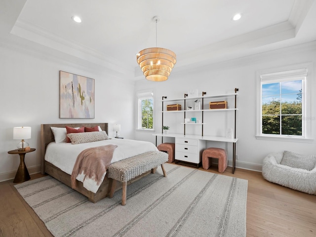 bedroom with a tray ceiling, ornamental molding, a chandelier, and light wood-type flooring