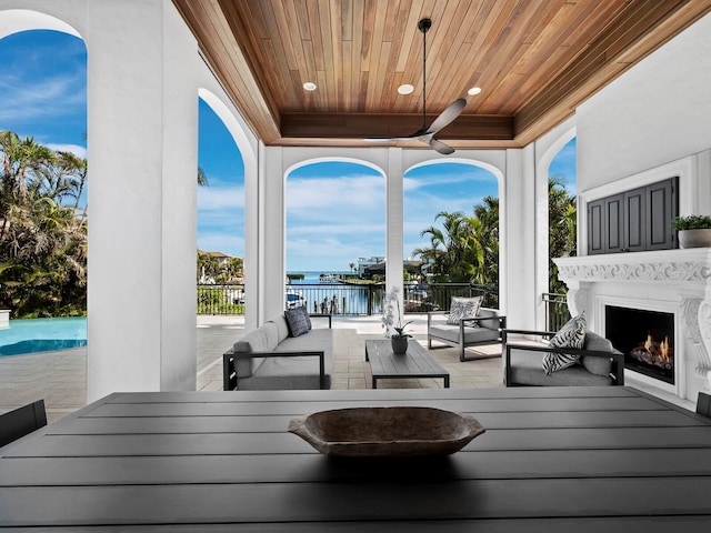 wooden deck featuring ceiling fan, an outdoor living space with a fireplace, and a water view