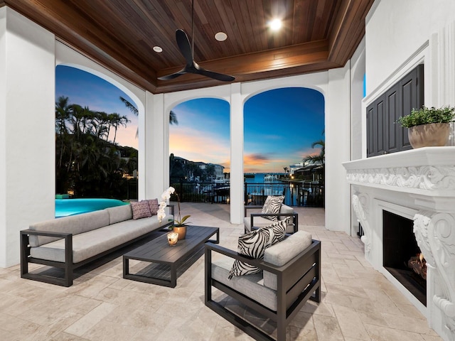 patio terrace at dusk with a water view, an outdoor living space with a fireplace, and ceiling fan