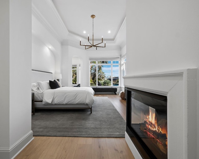 bedroom with hardwood / wood-style floors, a tray ceiling, ornamental molding, and a chandelier