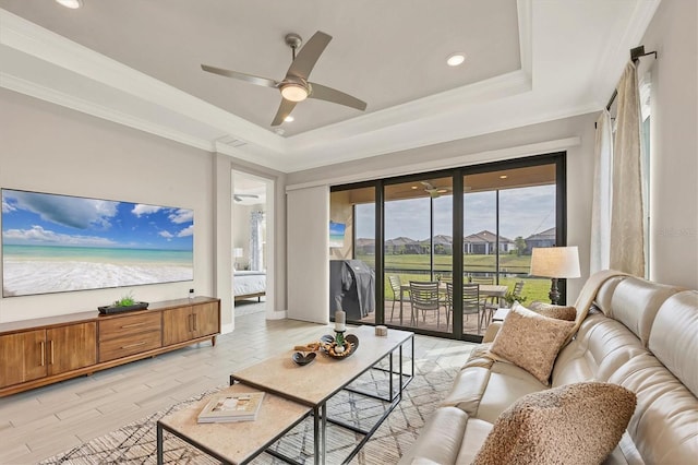 living room with ornamental molding, ceiling fan, light wood-type flooring, and a tray ceiling