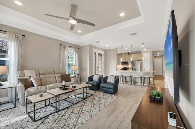 living room with a raised ceiling, ornamental molding, ceiling fan, and light wood-type flooring