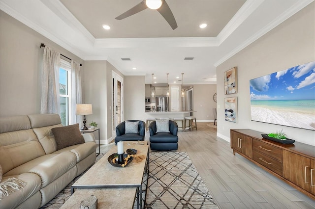 living room with a raised ceiling, ornamental molding, ceiling fan, and light hardwood / wood-style flooring