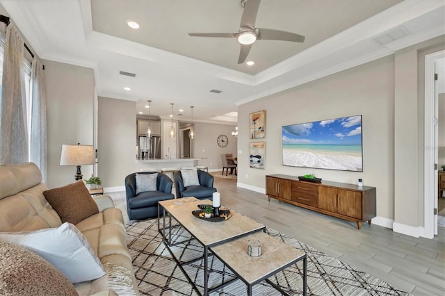 living room featuring ornamental molding, ceiling fan, light wood-type flooring, and a tray ceiling