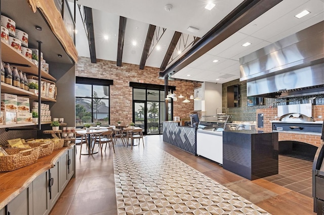 kitchen with tile patterned flooring, backsplash, a high ceiling, brick wall, and beamed ceiling