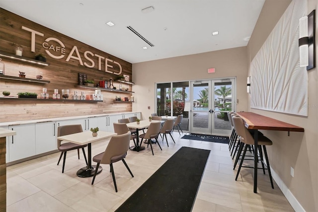 bar with french doors, wood walls, white cabinetry, tasteful backsplash, and light tile patterned floors