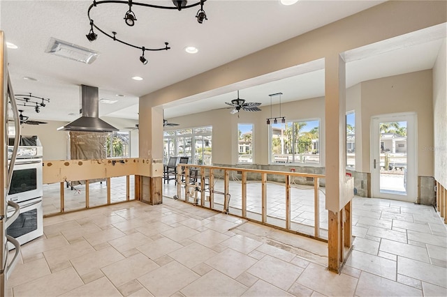 interior space with hanging light fixtures, ceiling fan, island range hood, and double oven