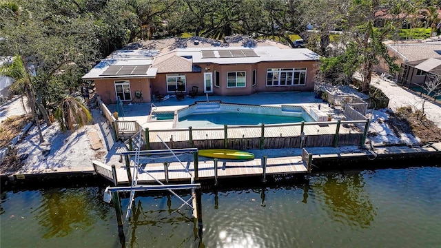 rear view of house with a water view, a pool with hot tub, a patio, and solar panels