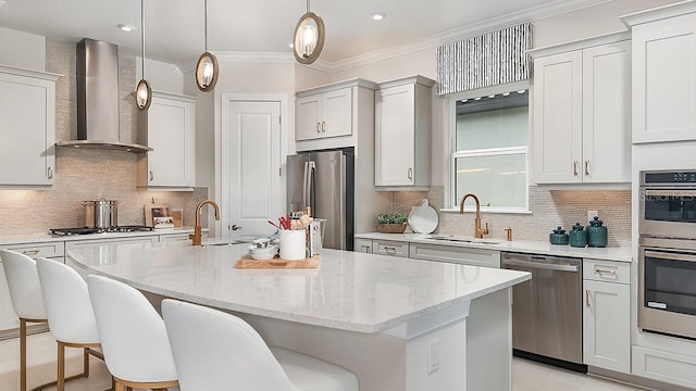 kitchen featuring stainless steel appliances, wall chimney range hood, an island with sink, and a sink