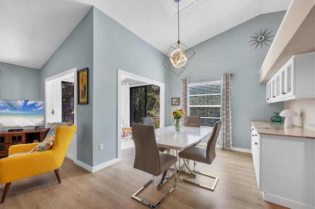 dining space featuring high vaulted ceiling, a textured ceiling, and light wood-type flooring