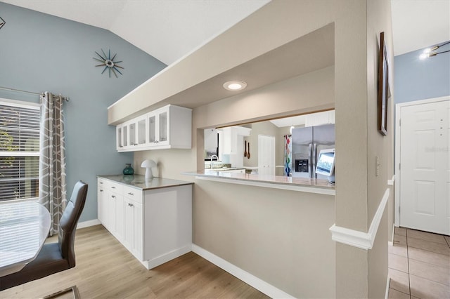 kitchen featuring white cabinetry, lofted ceiling, stainless steel fridge, and kitchen peninsula